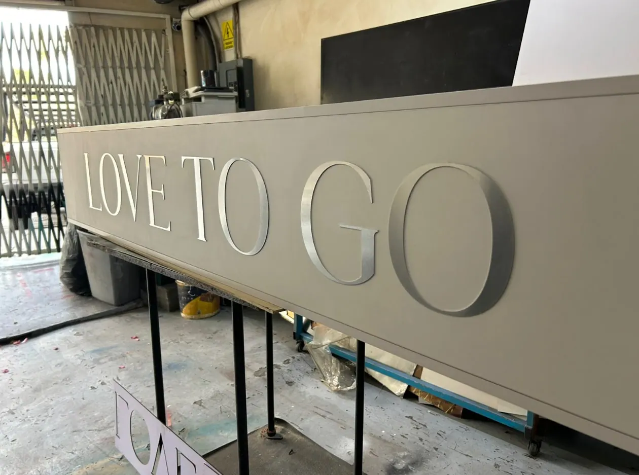 Anuncio de gran formato con letras metálicas en relieve, en proceso dentro de un taller