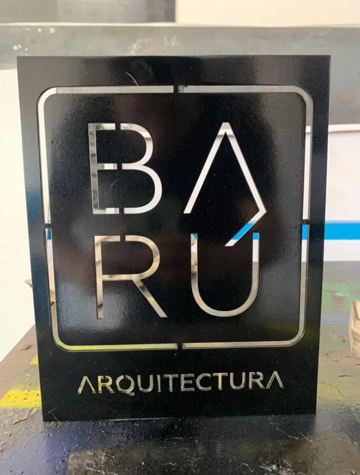 Letrero de acero negro con letras caladas sobre fondo espejo