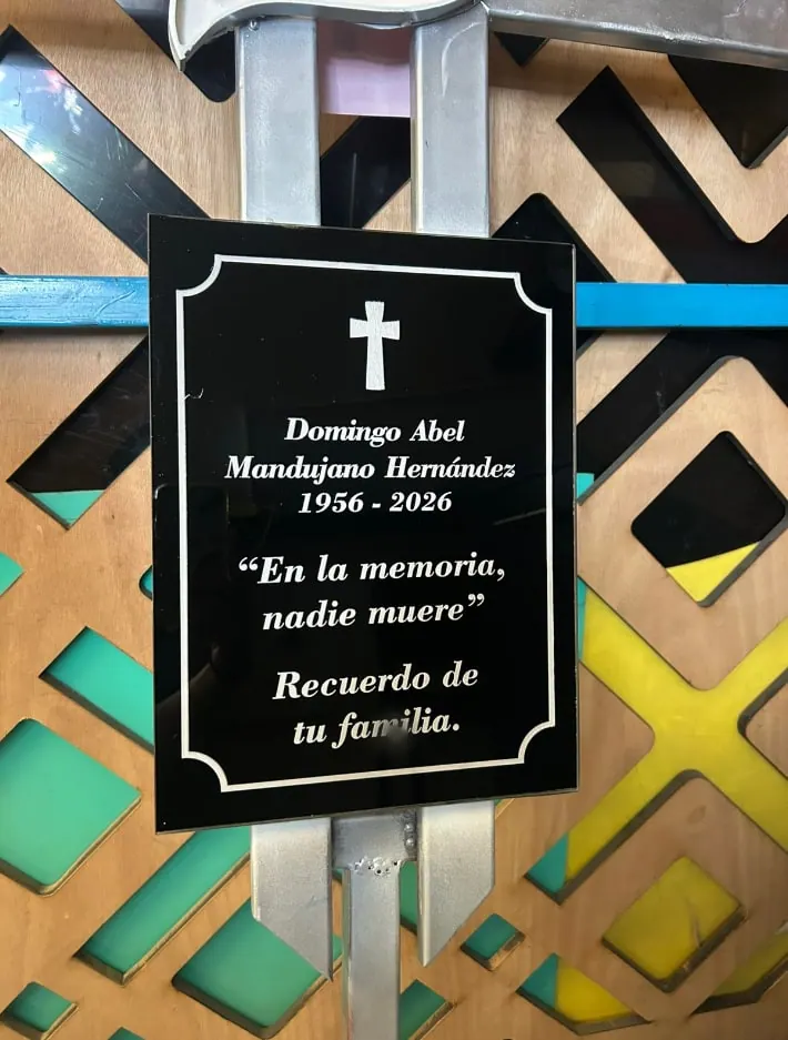 Placa negra con cruz, nombre y dedicatoria grabados